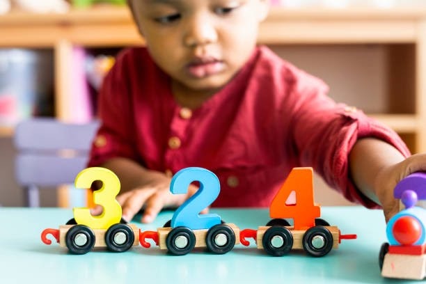 A toddler playing with colorful number train toys in a classroom